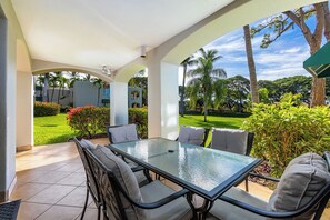 An outdoor patio with a glass-top table and chairs, surrounded by greenery and palm trees.