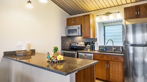 Una cocina con encimeras de granito, armarios de madera, electrodomésticos de acero inoxidable e iluminación colgante.
