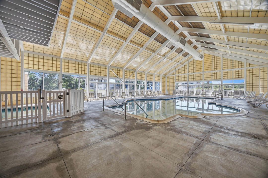 Une piscine intérieure dotée d’une paroi en verre, entourée de chaises longues et surmontée d’un plafond haut orné d’un motif en réseau.