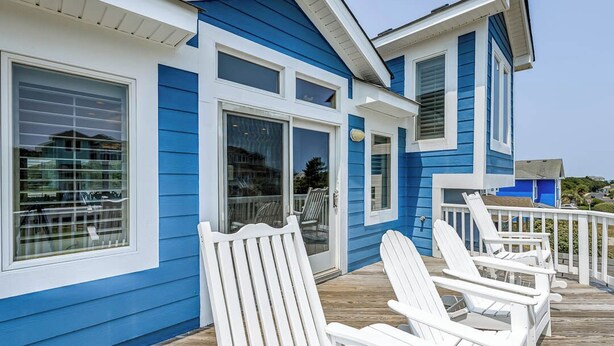 Una casa blu con decorazioni bianche, un pontile in legno e poltrone Adirondack bianche.