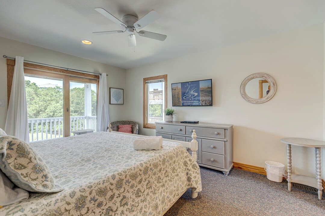 A bedroom with a bed, a dresser, a mirror, and a ceiling fan.