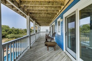 A covered wooden deck with a pool, wooden chairs, and a view of the pool and greenery.