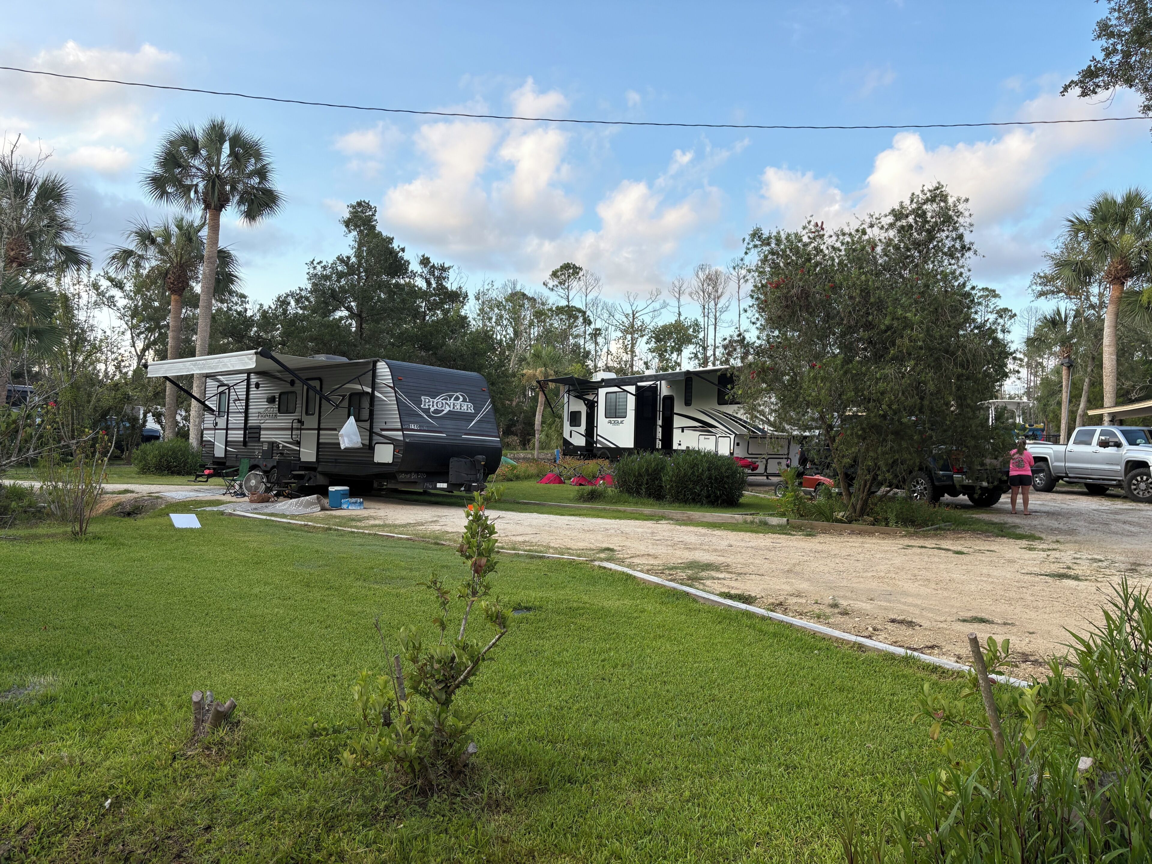 A campsite with two RVs, a truck, and a grassy area with trees.