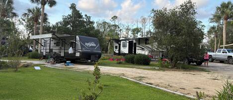 A campsite with two RVs, a truck, and a grassy area with trees.