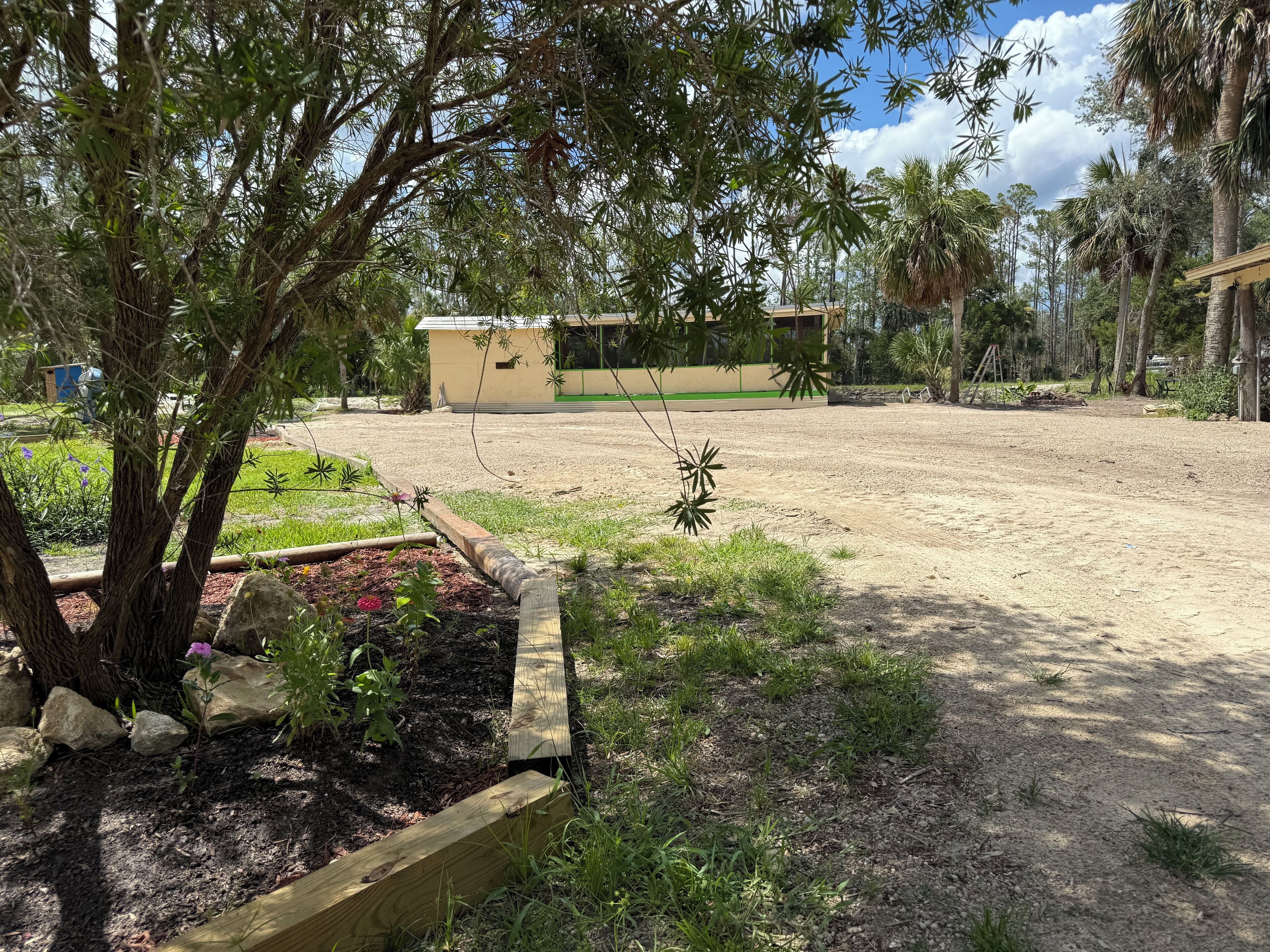 A spacious outdoor area with a sandy ground, surrounded by trees and a small building in the background.