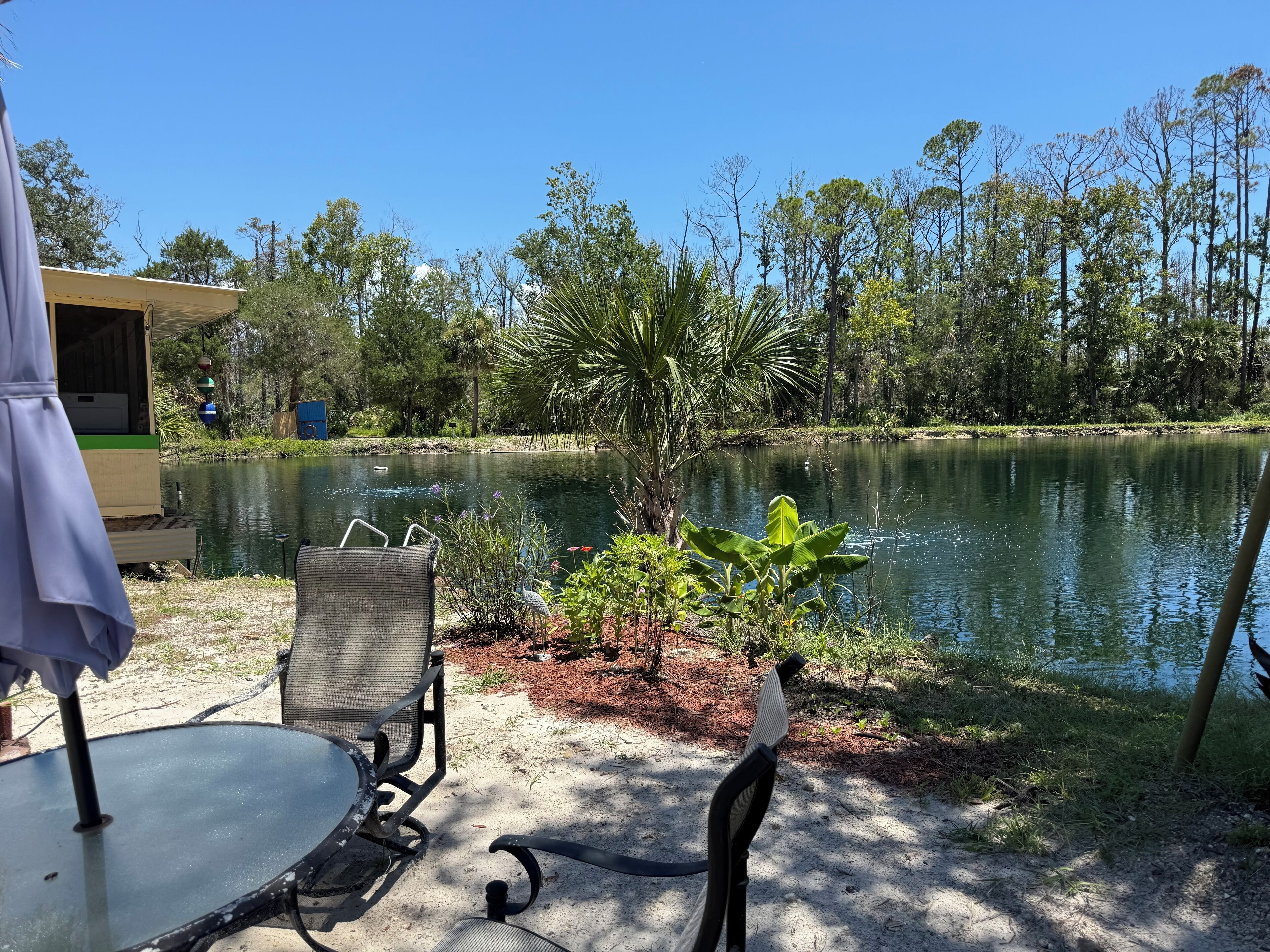 Une terrasse au bord du lac, avec une table et des chaises, entourée d’une végétation luxuriante et donnant sur un lac paisible.