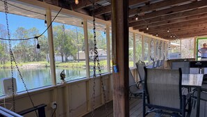 A covered outdoor seating area with a view of a lake, wooden deck, and hanging lights. - Lake Retreat of Steinhatchee- bring your RV to the place for fun and memories!! (Steinhatchee)