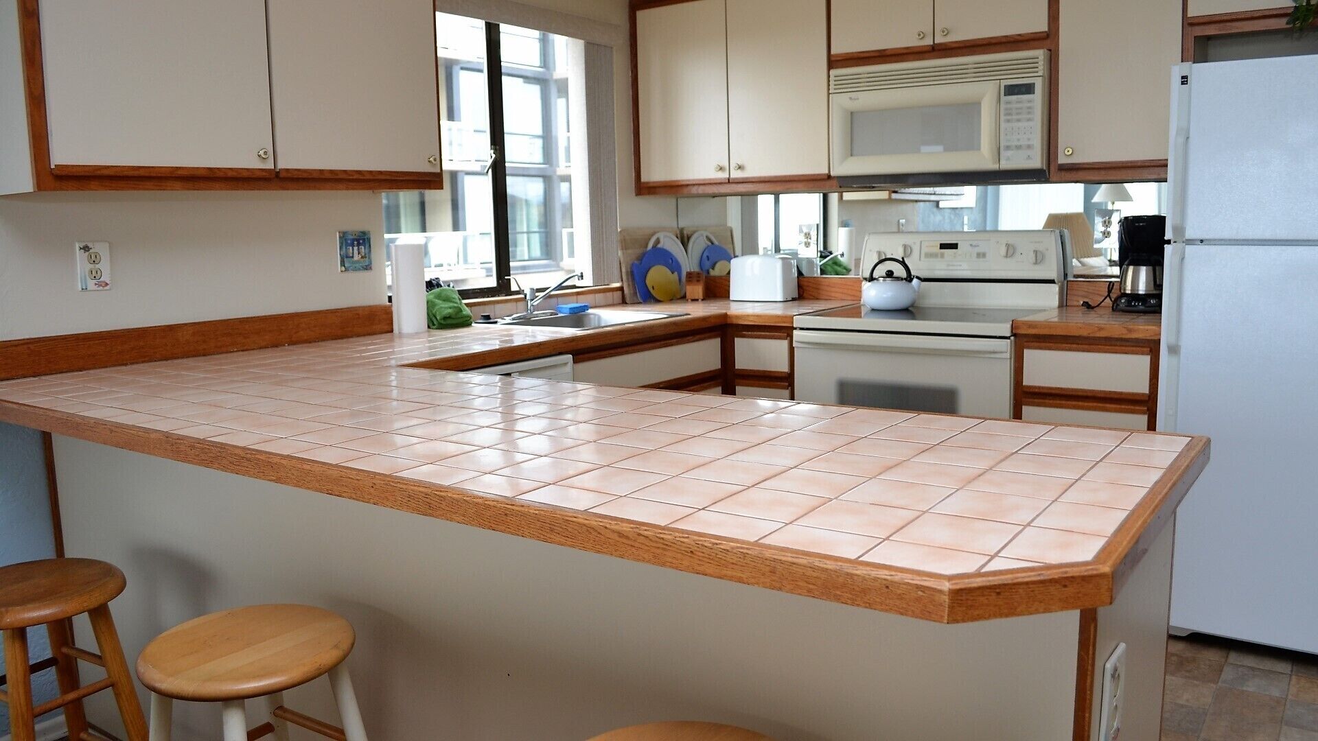 A kitchen with a central island, wooden stools, a microwave, stove, and a refrigerator.