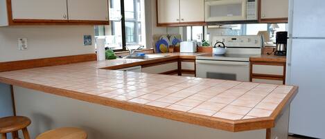 A kitchen with a central island, wooden stools, a microwave, stove, and a refrigerator.