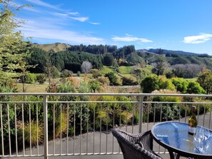 Un balcón con mesa y silla, con vistas a un paisaje pintoresco con colinas y árboles.