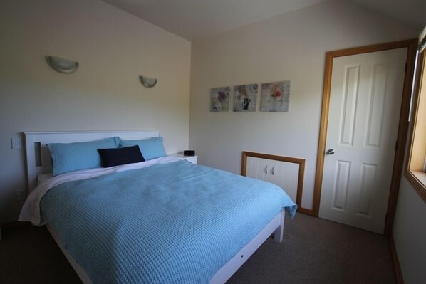 Un dormitorio con cama, mesita de noche, una puerta y decoración en la pared.