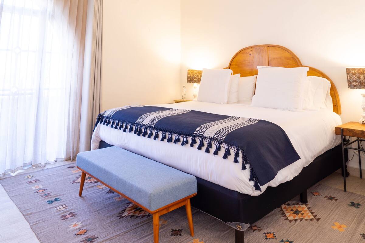 Ein ordentlich gemachtes Bett mit hölzernem Kopfteil, einer Bank am Fußende und einem gemusterten Teppich auf dem Boden.