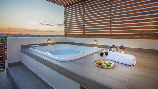Een dak terras met een jacuzzi, een dienblad met snacks en drankjes, en uitzicht op de stad bij zonsondergang.