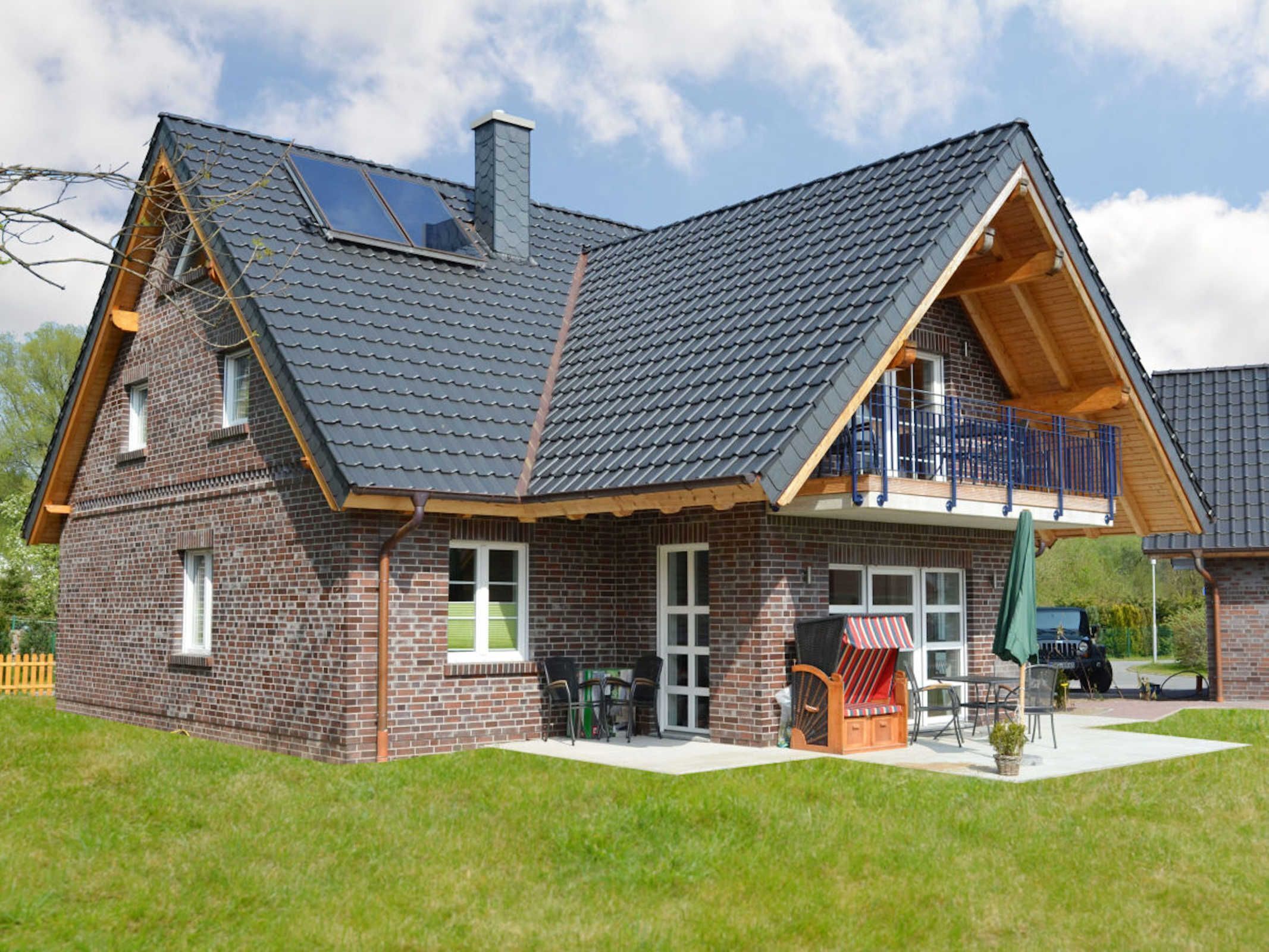 A two-story brick house with a sloped roof, a balcony, and a patio area with outdoor furniture.