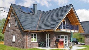 A two-story brick house with a sloped roof, a balcony, and a patio area with outdoor furniture. - Vacation apartment North Sea (OG) (Sellin)