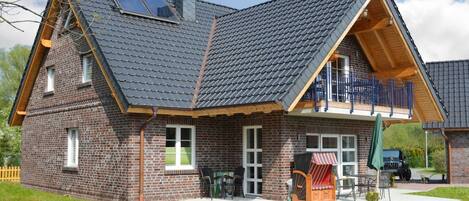 A two-story brick house with a sloped roof, a balcony, and a patio area with outdoor furniture.