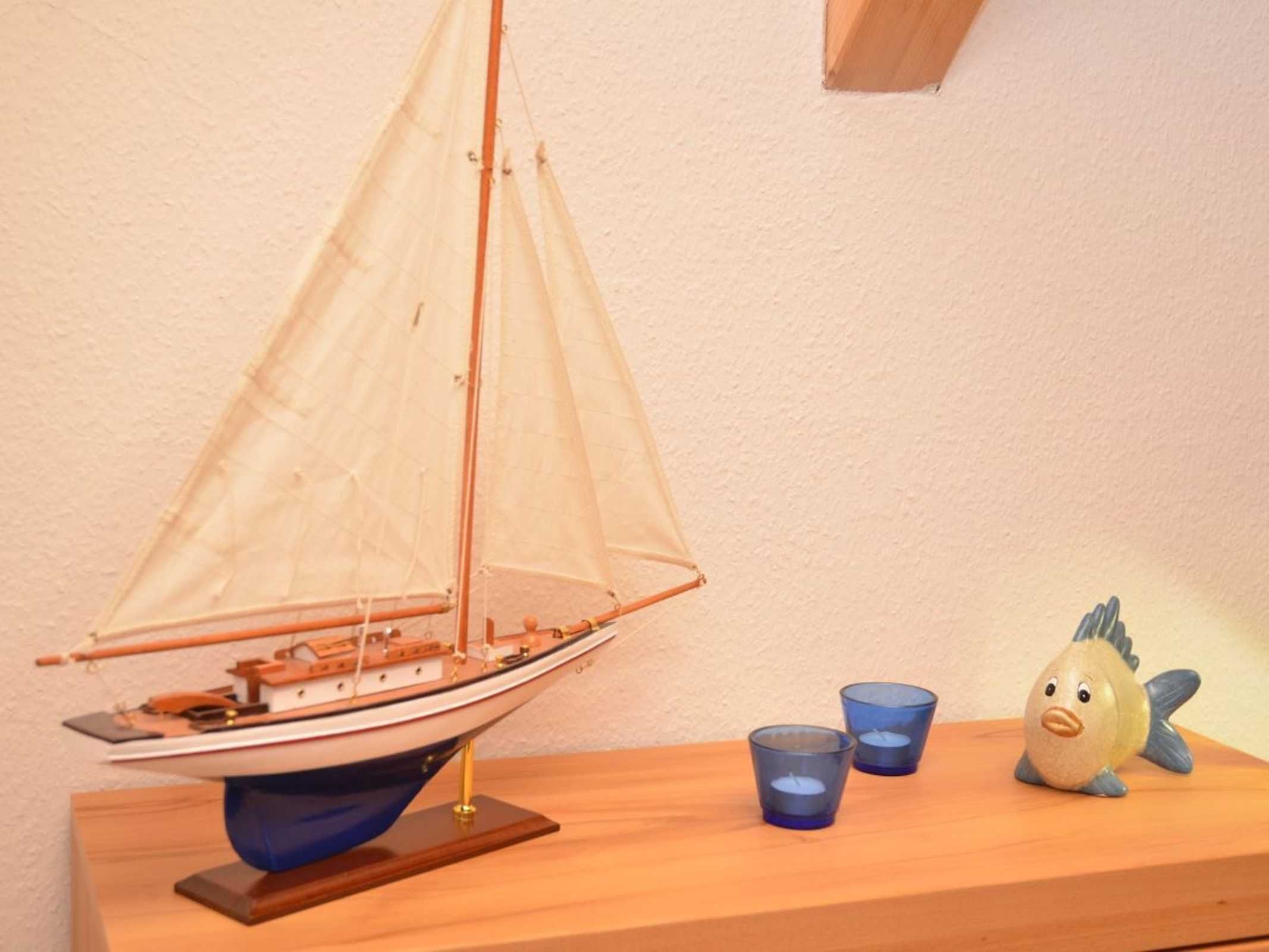 Un velero de juguete sobre un soporte de madera, dos tazas azules pequeñas y un pez de juguete.
