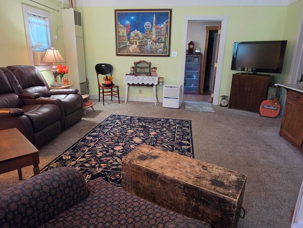 A living room with a sofa, a rug, a wooden chest, a television, and a painting on the wall.