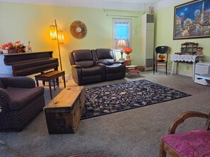 Una sala de estar con un piano, sofá de cuero, sillón estampado y una alfombra decorativa.