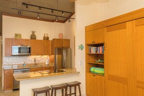 A kitchen with wooden cabinets, stainless steel appliances, a granite countertop, and a small island with stools. -  Maui Magic A206 AC BEACHFRONT Napili Bay/ATTN: Cleaning fee added AFTER booking (Lahaina)