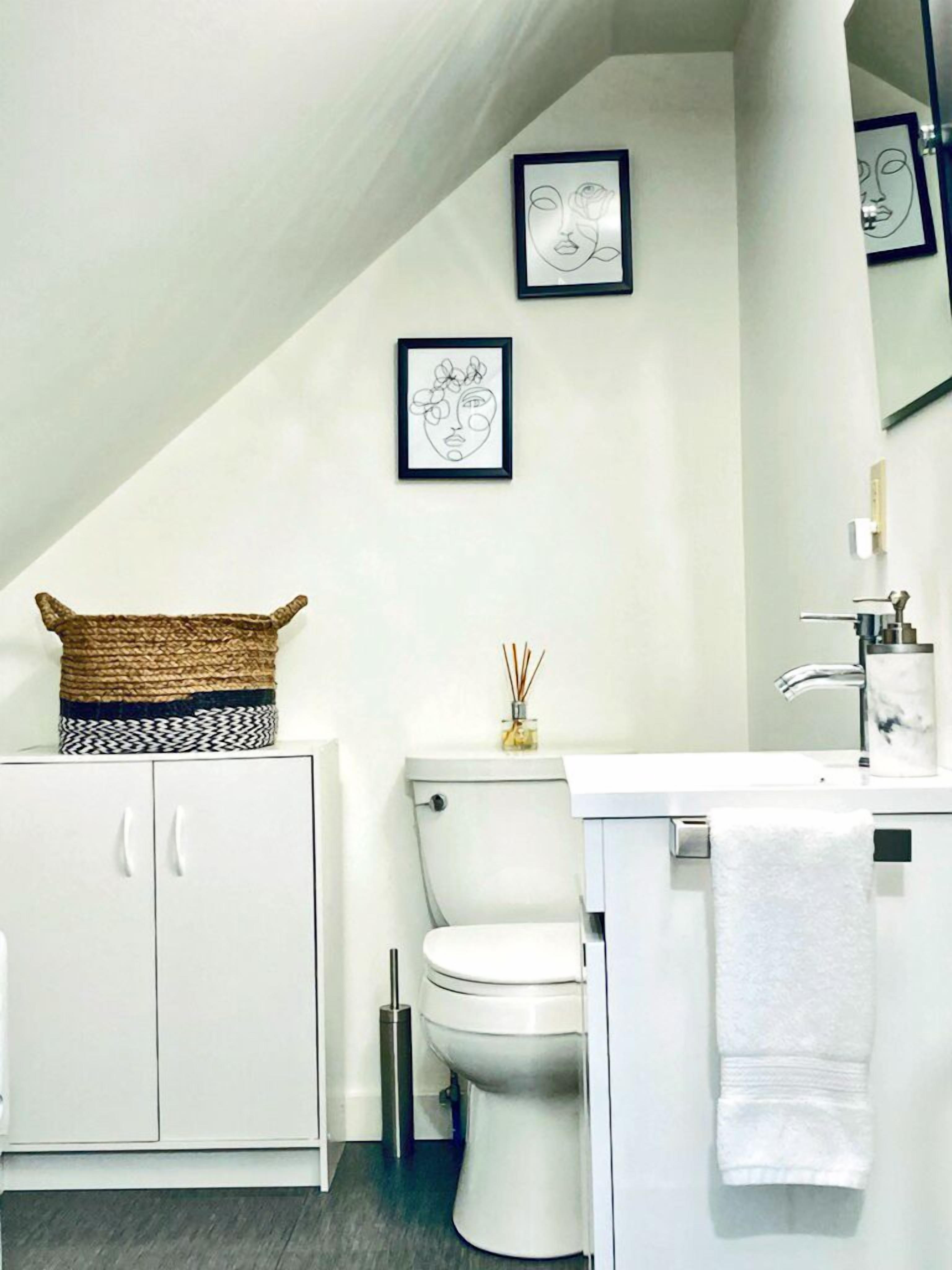 A modern bathroom with a white toilet, a white sink, and a towel hanging on the wall. There are two framed artworks on the wall above the toilet.