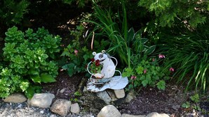 Un giardino con una vasca per uccelli in metallo rustica, circondata da diverse piante verdi e rocce.