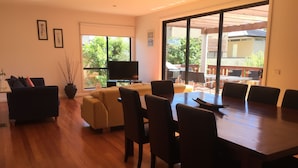 A spacious living room with a large wooden dining table, comfortable sofas, and a flat-screen TV. - Just 30 seconds walk to DROMANA Swimming BEACH, WIFI, Parking, heating & cooling (Dromana)
