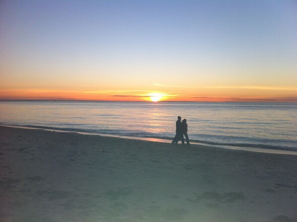 Escena de playa con un atardecer sobre el océano.