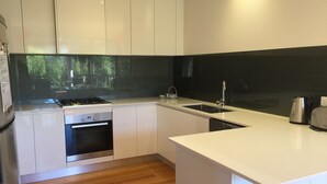 A modern kitchen with white cabinetry, a black backsplash, a stainless steel kettle, and a built-in oven. - Just 30 seconds walk to DROMANA Swimming BEACH, WIFI, Parking, heating & cooling (Dromana)