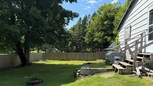 A backyard with a wooden fence, a tree, and a house with a visible staircase. - Rustic intown country apartment on the Moosehead trail (Sangerville)