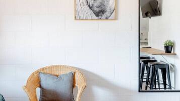 A room with a wicker chair, a framed picture on the wall, and a mirror reflecting a kitchen area.