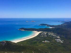 An aerial view of a coastal area with a beach, forested hills, and clear blue waters.
