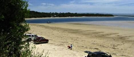 Una playa con un coche aparcado y una mochila sobre la arena.