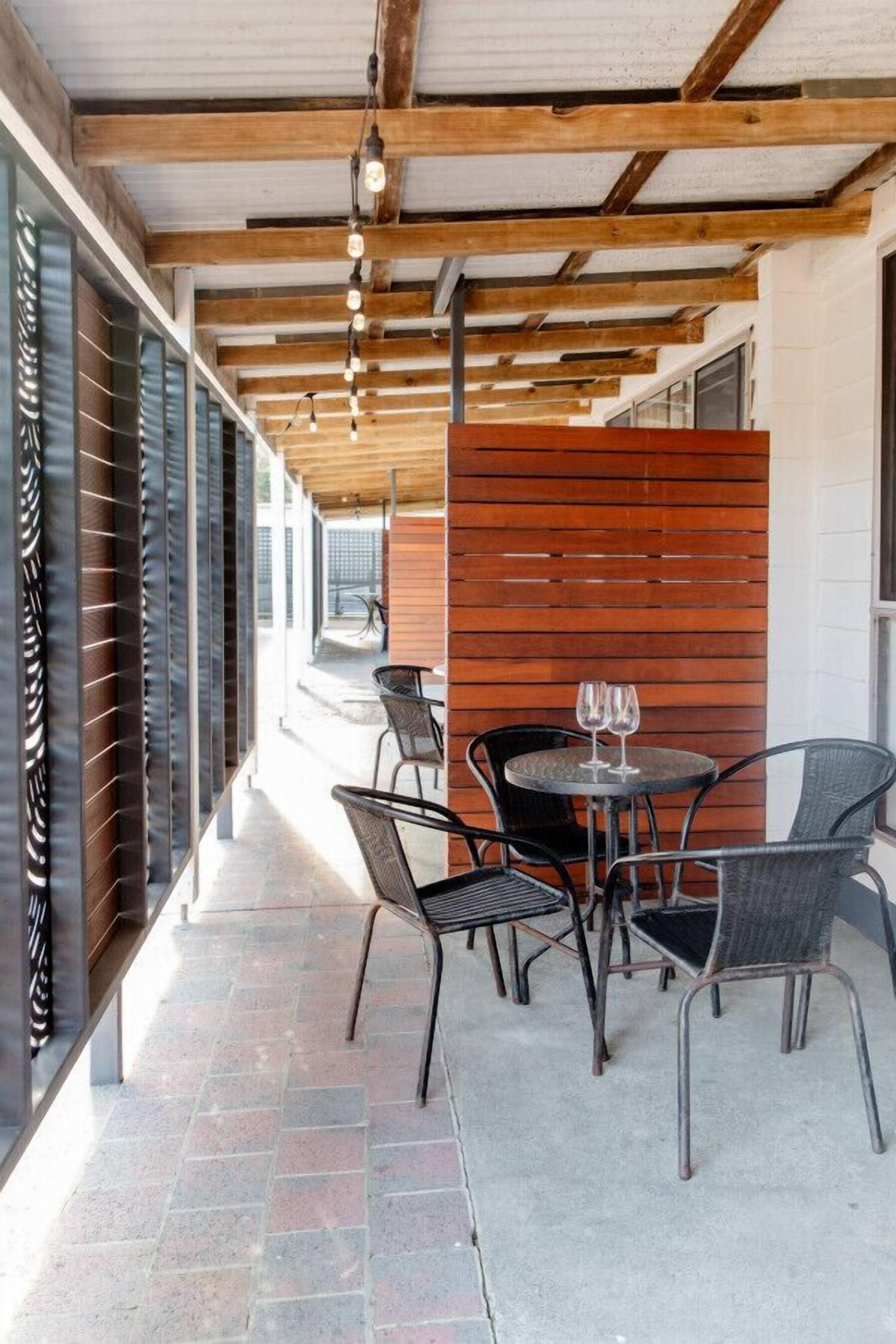 An outdoor seating area with tables and chairs, a wooden partition, and a view of the street.