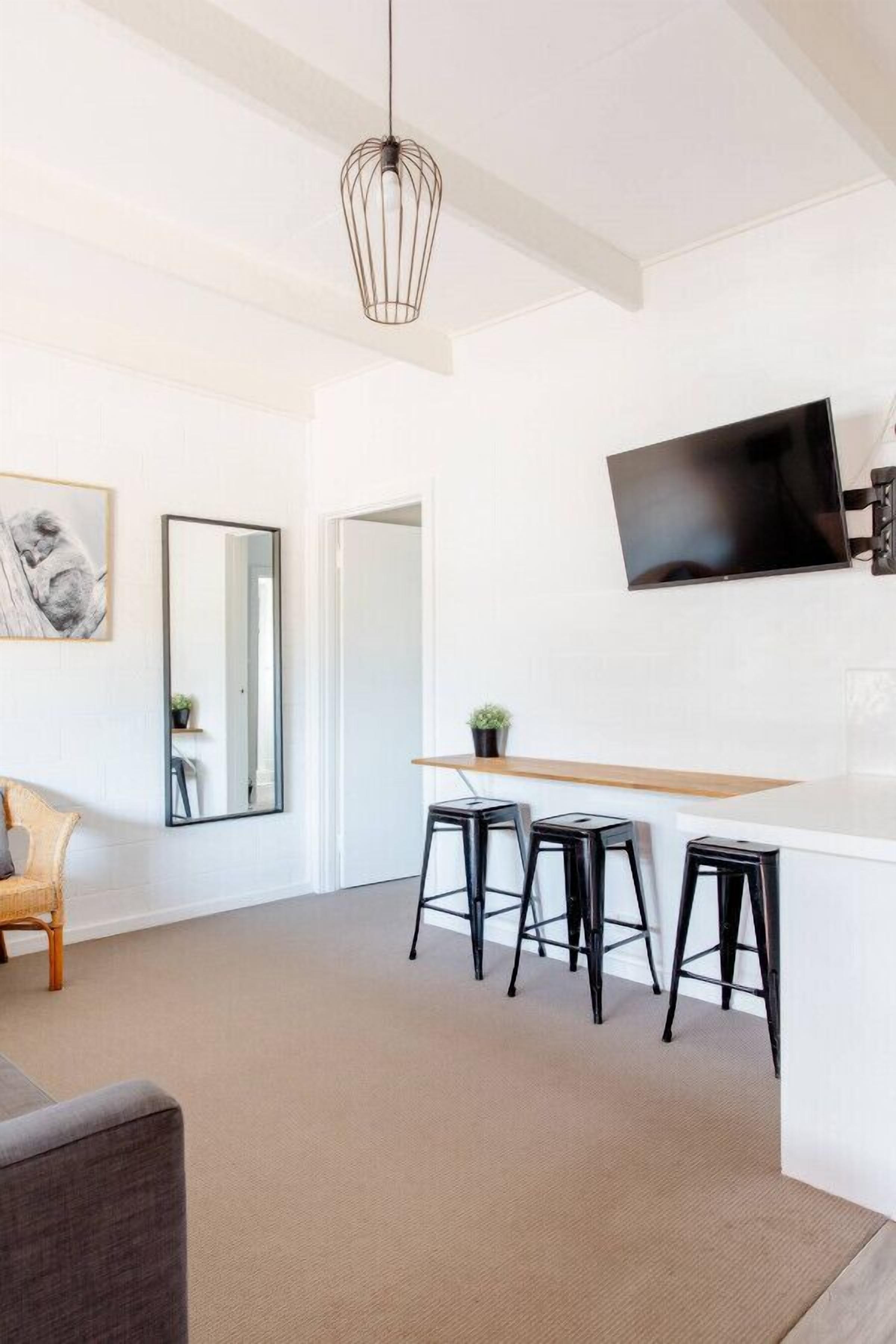 A modern living room with a flat-screen TV, a dining area with stools, and a large mirror.