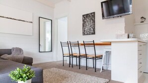 A modern living room with a grey sofa, a coffee table with a plant, a dining area with chairs and a table, and a TV mounted on the wall.