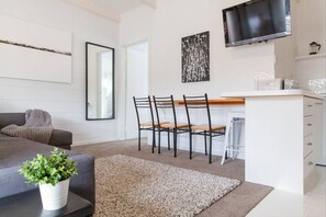 A modern living room with a grey sofa, a coffee table with a plant, a dining area with chairs and a table, and a TV mounted on the wall. - Prom Coast 3 ~ Beach Getaway ~ Stunning Beach! (Sandy Point)