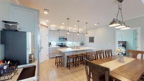 A modern kitchen with a central island, wooden chairs, and pendant lighting.