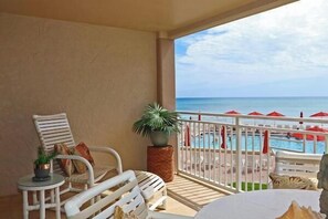 A balcony with white wicker furniture, a small table with a plant, and a view of a pool and beach. - Location, location, location. Keep a close eye on the kids pool side, from this 2nd floor 2/2 condo (New Smyrna Beach)