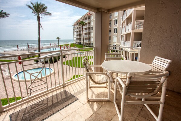 A balcony with a pool, chairs, and a view of the beach and ocean.