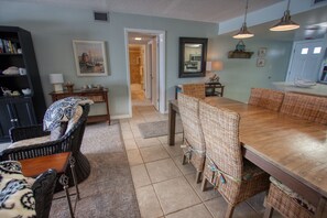 A spacious living area with a dining table, wicker chairs, a bookshelf, and a painting on the wall.