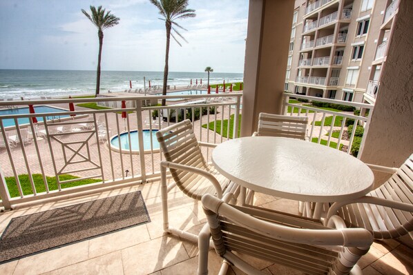 A balcony with a pool, chairs, and a table overlooking the beach and ocean. - Location, location, location. Keep a close eye on the kids pool side, from this 2nd floor 2/2 condo (New Smyrna Beach)
