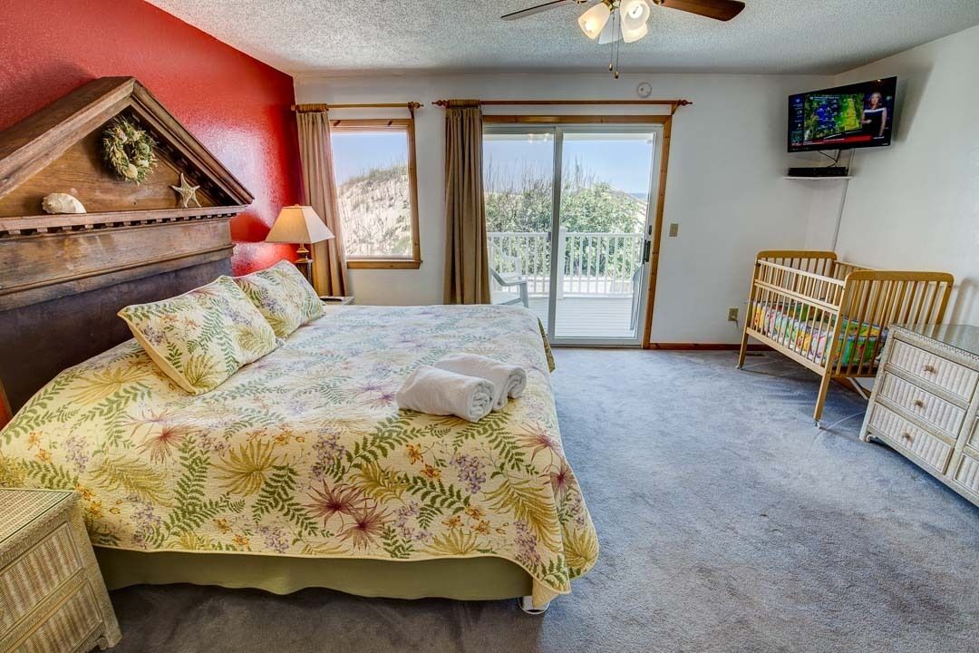 Una camera da letto con un letto, una cassettiera in legno, una culla, una televisione e un balcone con vista.