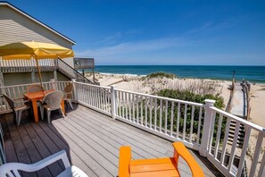 Une terrasse en bois avec des meubles d’extérieur, un espace salon couvert et une vue sur la plage et l’océan.