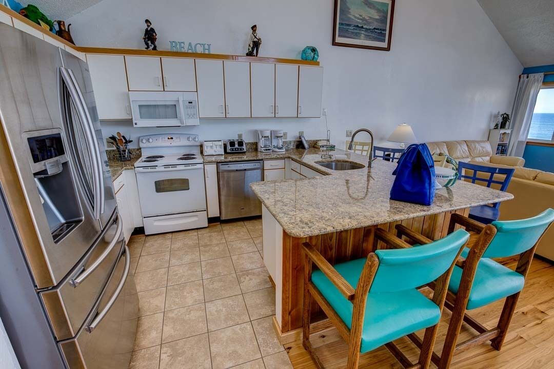 Una cocina compacta con armarios blancos, encimera de granito y sillas color turquesa.