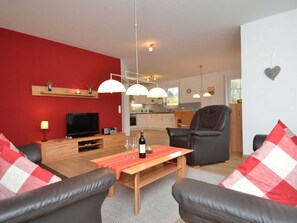 Ein modernes Wohnzimmer mit roter Akzentwand, einem Holztisch, Ledersofas und einem Fernseher.