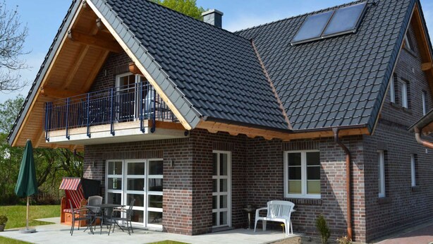 A two-story house with a sloped roof, a balcony, and a patio area with outdoor furniture. - Vacation apartment Baltic Sea (ground floor) - barrier-free (Sellin)
