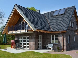A two-story house with a sloped roof, a balcony, and a patio area with outdoor furniture. - Vacation apartment Baltic Sea (ground floor) - barrier-free (Sellin)