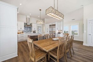 A spacious kitchen with white cabinetry, a central island, and wooden chairs around a dining table.