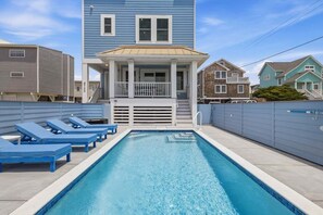 A swimming pool with lounge chairs, a covered deck, and a two-story building with a balcony.